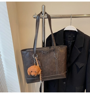 Detail of dark brown tote bag featuring white contrast stitching and a plush dog charm