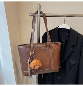 Detail of a brown leather tote bag with a cute curly dog charm and striped tassels