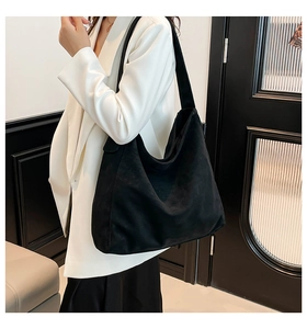 Detail of minimalist black suede hobo tote with wide shoulder strap on model in white suit