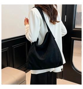 Side view of a large black suede tote bag shown on a model in a modern interior