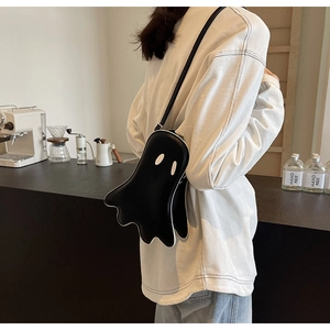 Close-up of a ghost-shaped black leather crossbody bag worn in a modern cafe setting