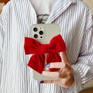 Close-up of a large red velvet 3D bow on a transparent phone case held by hand