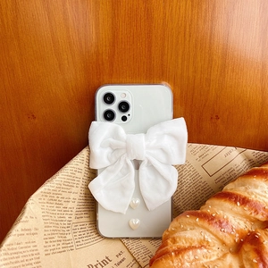 Detail of iPhone case featuring velvet white bow and pearl heart charms on wood texture