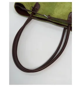 Close-up of green faux suede tote bag with brown synthetic leather strap and metal buckle