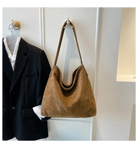 Brown suede hobo tote bag displayed on wall beside a black business blazer suit