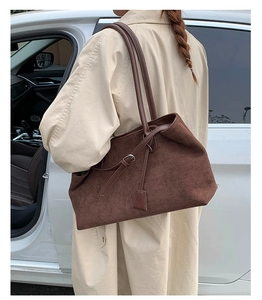 Detailed view of deep brown suede tote bag carried by model in a stylish beige trench coat
