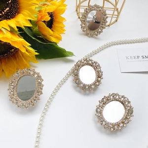 Detail of four oval rhinestone mirror phone grips with sparkling gold frames on floral background
