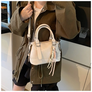 Detail of minimalist beige Boston bag with letter embossing and tassel on a green trench coat
