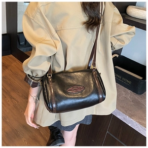 Detail of black crossbody bag with red logo patch and brown strap on a khaki trench coat
