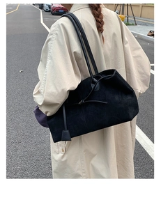 Detail of matte black suede tote bag with slim straps styled on a beige trench coat