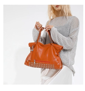 Detail der hellorangen Shopper-Tasche mit seitlicher Fransenquaste und silbernen Nieten