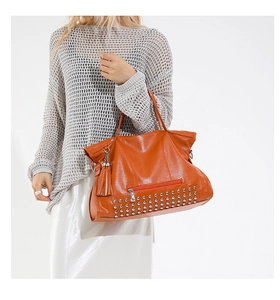 Detailaufnahme der orangen Ledertasche mit Silbernieten und Quasten am Reißverschluss