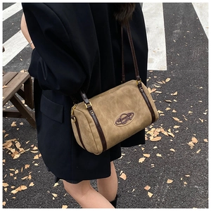 Detail of a vintage-style suede Boston bag in earthy tones worn over a black coat