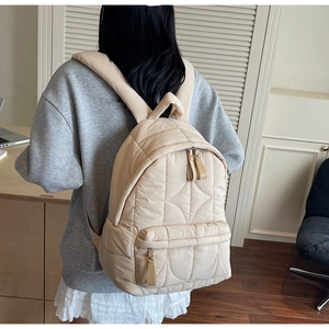 Detail view of cream quilted puffer backpack featuring geometric stitching and double zippers