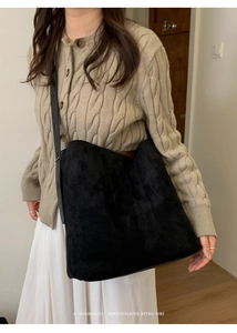 Detail einer schwarzen minimalistischen Wildleder-Einkaufstasche an einem Model im Innenraum