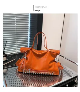 Detail der orangefarbenen Tragetasche aus Leder mit Nieten und Quasten-Anhänger