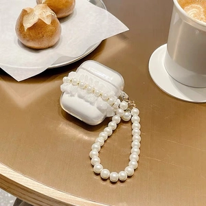 Detailed view of white lace AirPods case with large pearl wrist strap on wooden table