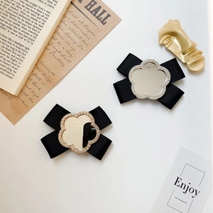 Close-up of black ribbon bow hair clips with rhinestone mirror center on white book
