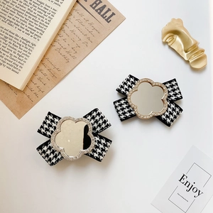 Macro view of bow-shaped phone grip with houndstooth fabric and crystal flower mirror detail