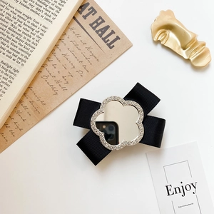 Detail of a black bow phone grip with a floral rhinestone mirror on a vintage aesthetic background