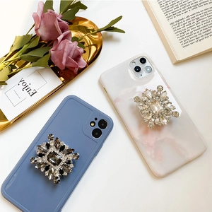 Close-up of sparkling rhinestone phone socket grip on stylish marble and matte cases