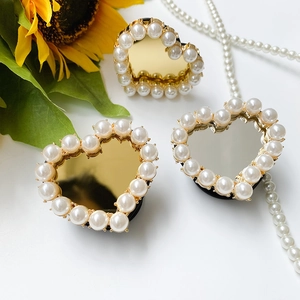 Detail view of heart-shaped mirror phone grips with white pearls in gold and silver finish