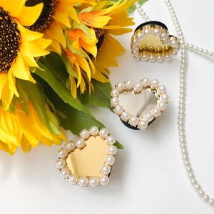 Detailed view of heart-shaped mirror phone grips with pearls in gold and silver finish