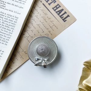 Close-up of a silver hat brooch with woven texture and bow detail on vintage paper