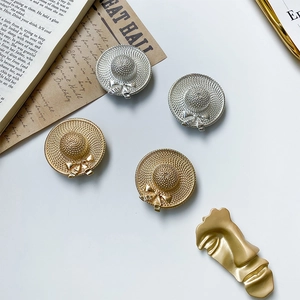 Close-up of golden and silver hat-shaped earrings with woven texture and bow details