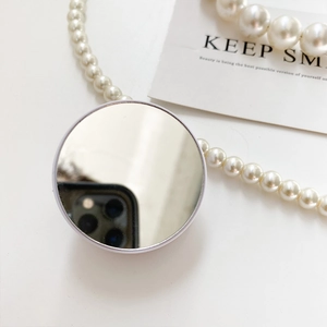Detail of white heart-shaped mirror phone grip with pearl necklace on a minimalist desk