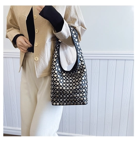 Détail d'un sac cabas punk noir orné de rivets métalliques argentés porté à l'épaule