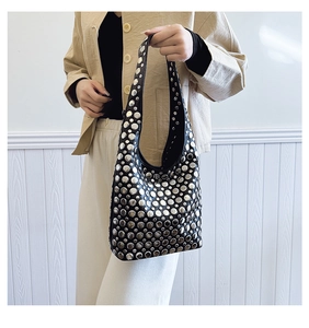 Détail d'un sac hobo en cuir noir avec clous argentés porté par un mannequin en tenue décontractée
