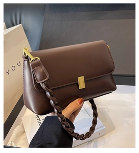 Detail of dark brown leather crossbody bag with gold metal buckle and woven shoulder strap