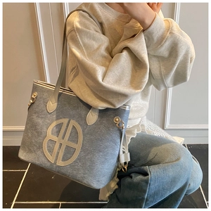 Detail of grey-blue textured tote bag featuring a large circular hollow logo and cream strap