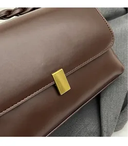 Macro detail of dark brown leather handbag with gold metal clasp and woven handle
