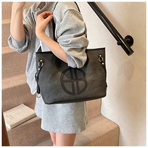 Detail view of large tote bag with circular embossed logo and gold hardware accents