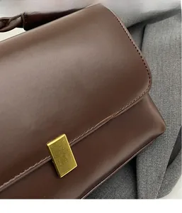 Close-up of matte dark brown leather bag showing gold buckle and stitching details