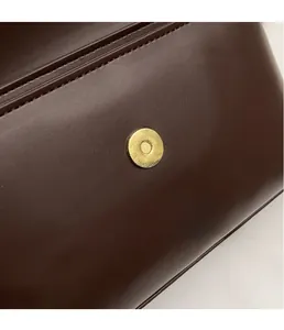 Close-up of golden textured magnetic buckle on premium dark brown leather shoulder bag