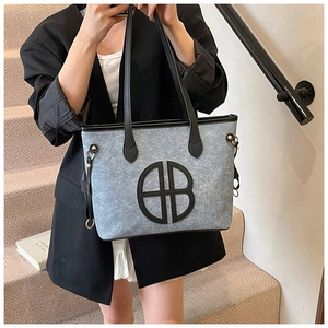 Detail of grey felt tote bag with black leather round patch and shoulder strap detail