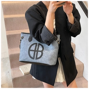 Detail of grey fabric tote bag featuring a large black circular logo and leather trim