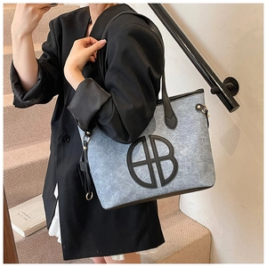 Close-up of grey felt tote bag with black leather straps and circular HB logo detail