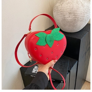Détail du sac fraise rouge avec des clous argentés et des feuilles vertes à paillettes
