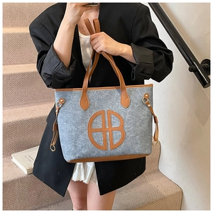 Detail of grey felt tote bag featuring brown leather AB logo and decorative side buckles