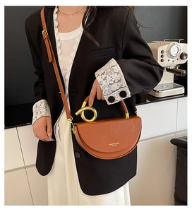 Detail of brown half-moon crossbody bag with golden metal knot handle and leather texture