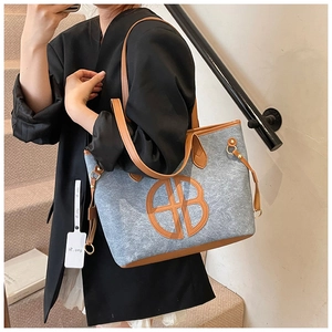 Detail of blue felt tote bag with brown leather trim and large circular logo on the side
