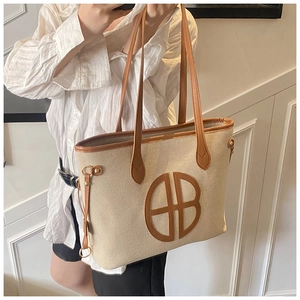 Detail of off-white canvas tote bag with brown leather trim and circular logo on shoulder