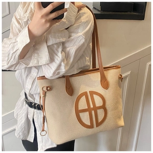Detail of canvas tote bag with brown leather trim and prominent front logo patch