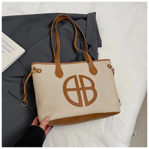 Detail of canvas tote bag with brown leather base and central AB logo embroidery