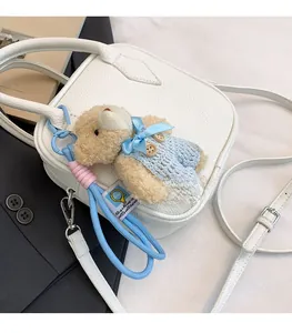 Detail of white lychee leather square bag with brown plush bear charm on grey blazer