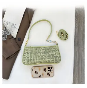 Detail view of green woven checkerboard bag showing compact size compared to a phone